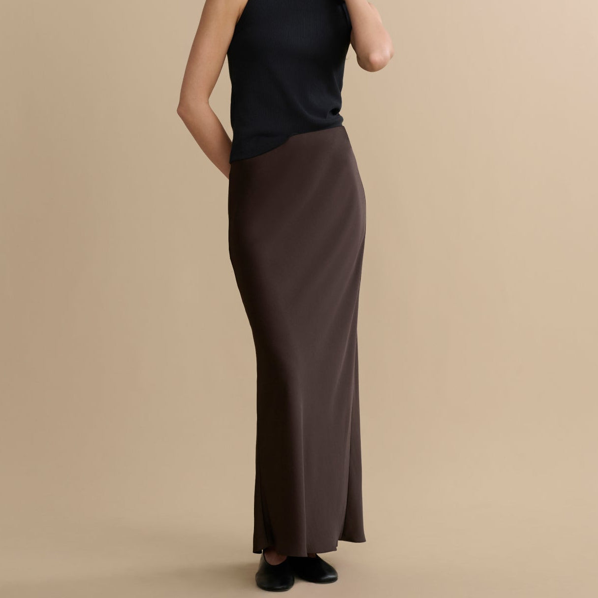Woman wearing a black sleeveless top and brown skirt on a beige background