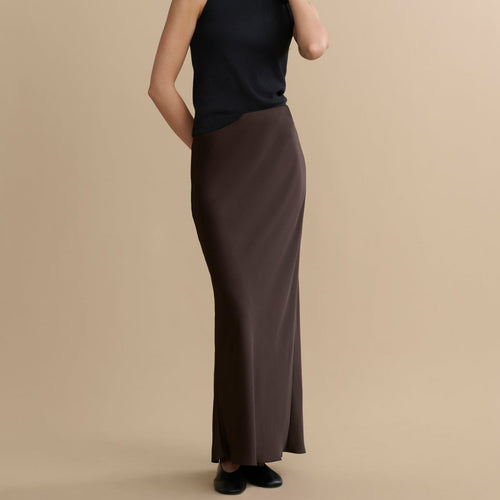 Woman wearing a black sleeveless top and brown skirt on a beige background