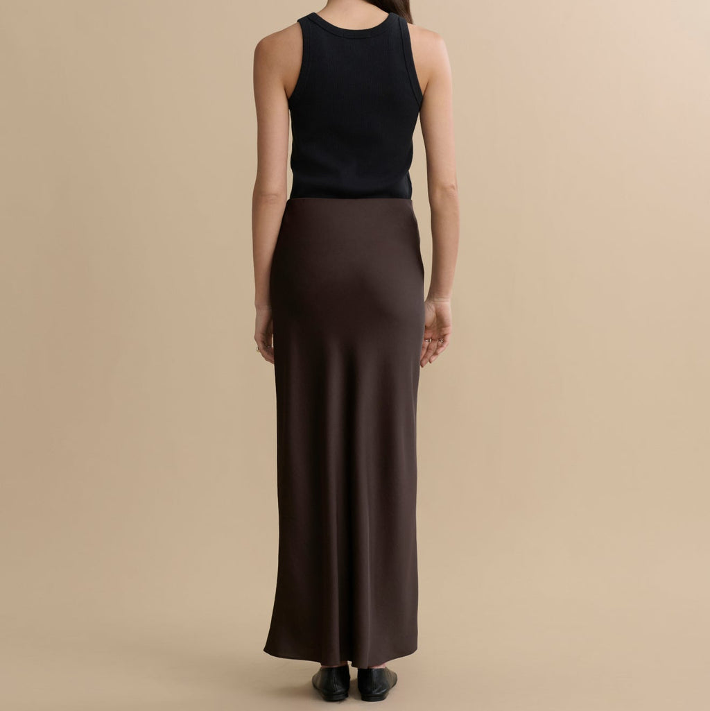 Woman wearing a black sleeveless top and brown skirt on a beige background