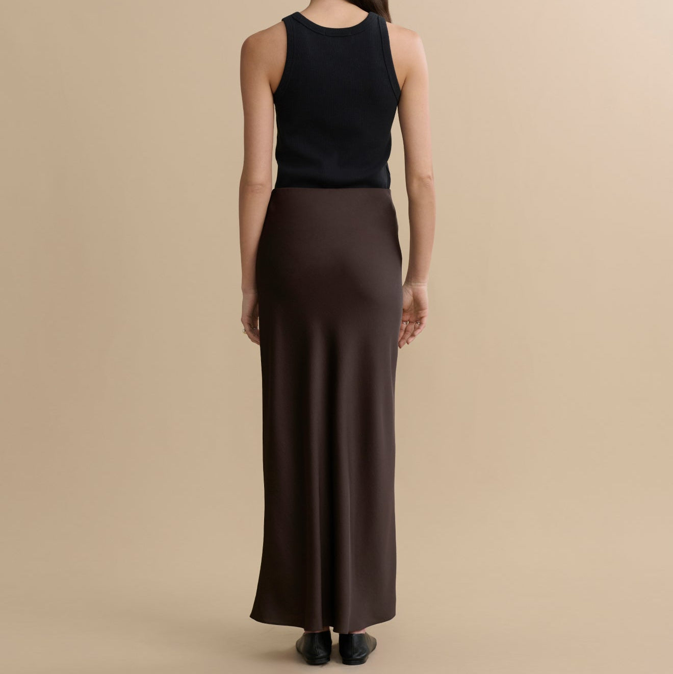 Woman wearing a black sleeveless top and brown skirt on a beige background