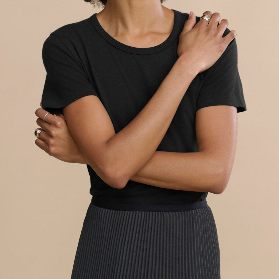 Woman wearing a black t-shirt and pleated skirt against a beige background