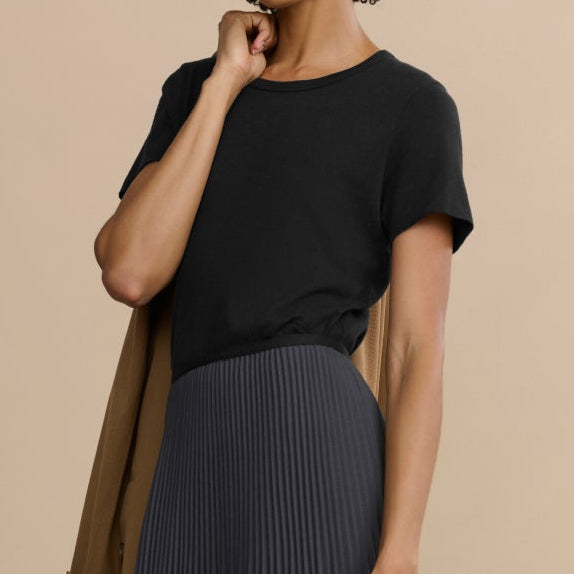Woman wearing a black top and long dark gray pleated skirt on a beige background