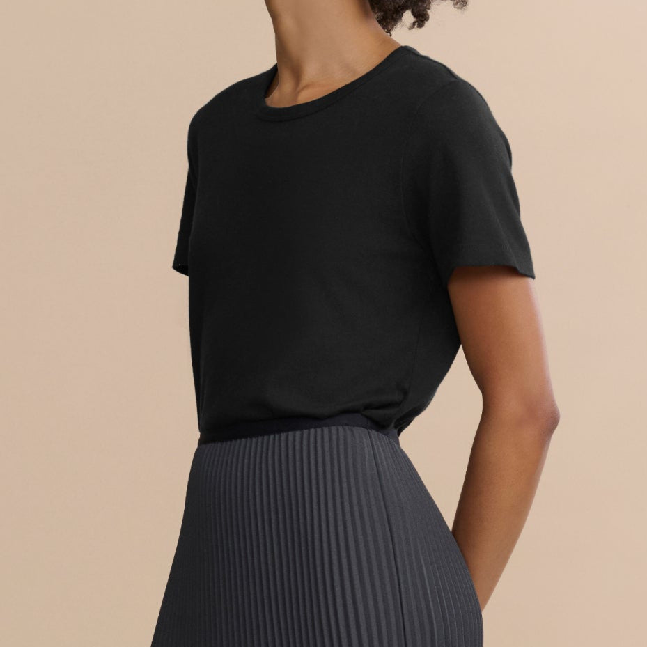Woman wearing a black top and pleated skirt against a beige background
