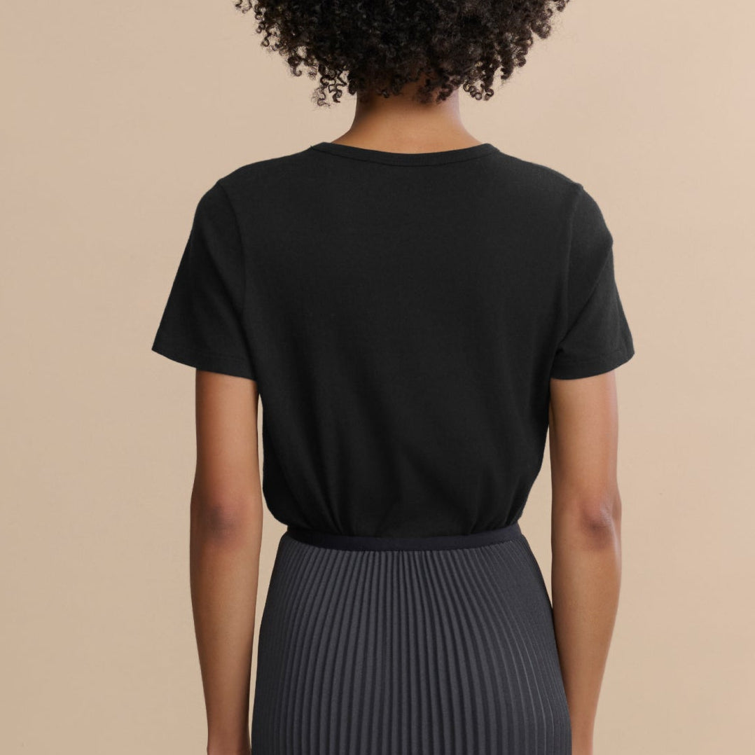 Person wearing a black t-shirt and pleated skirt on a beige background