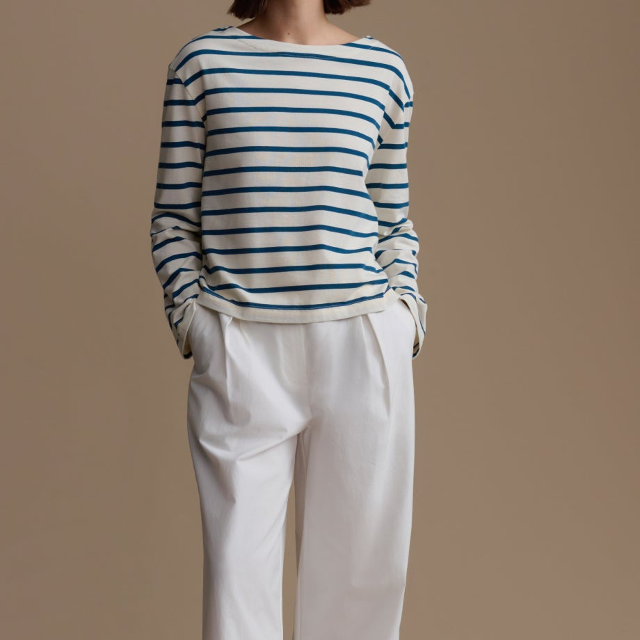 Woman wearing a striped sweater and white pants against a beige background