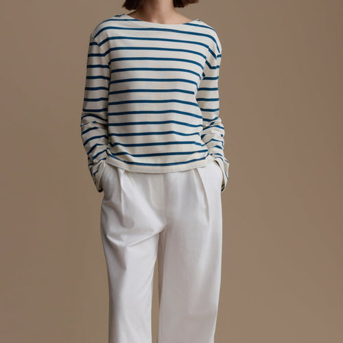 Woman wearing a striped sweater and white pants against a beige background