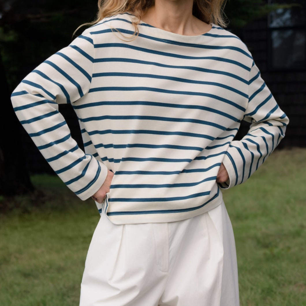 Woman wearing a striped sweater and white pants standing outdoors.