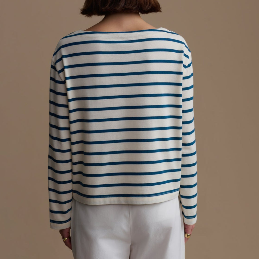 Person wearing a striped sweater and white pants against a beige background