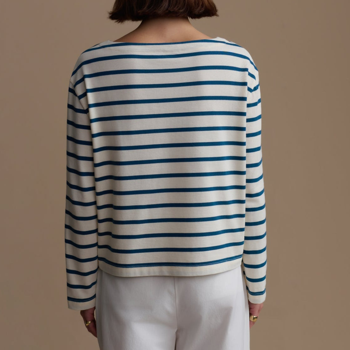 Person wearing a striped sweater and white pants against a beige background