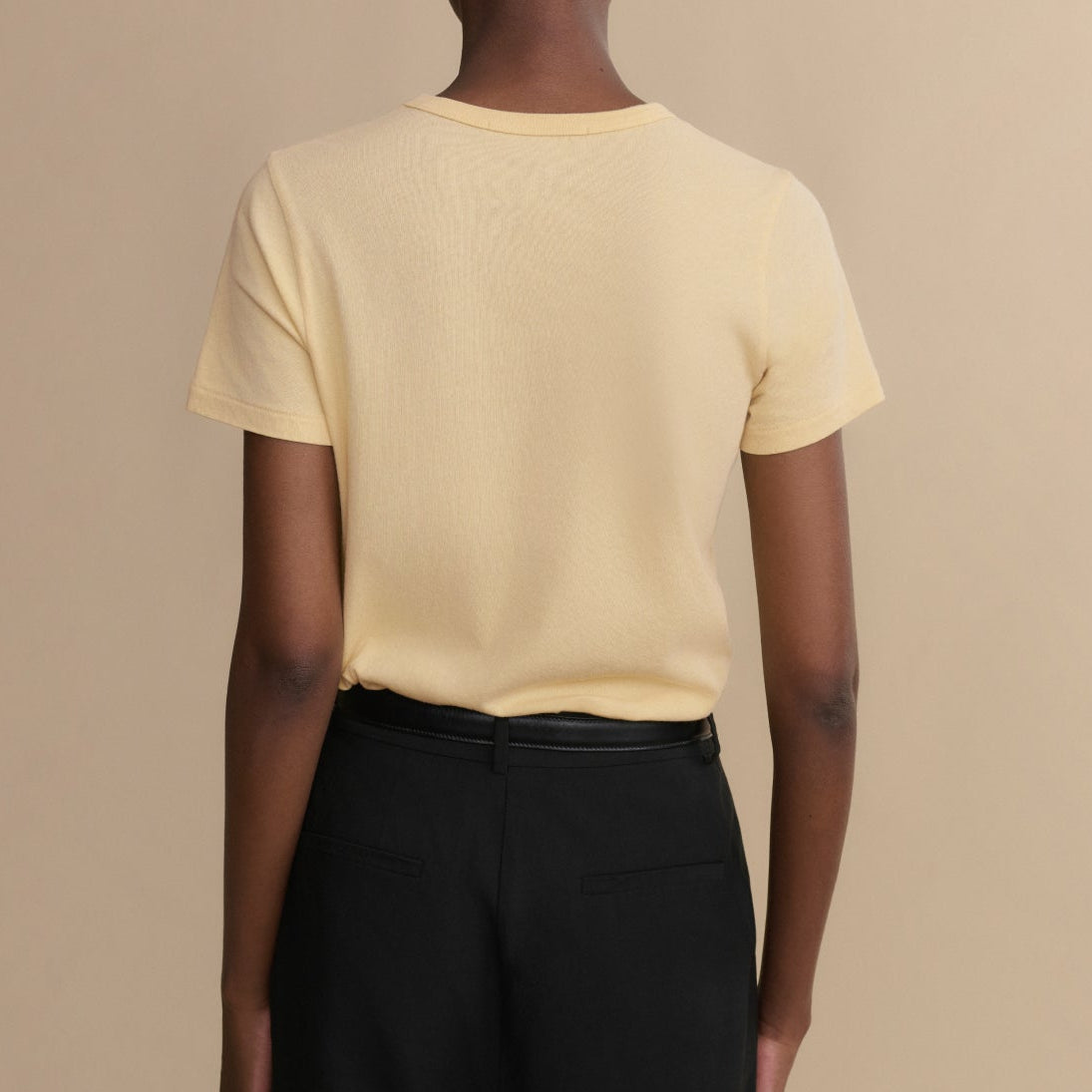 Person wearing a light yellow t-shirt and black pants against a beige background