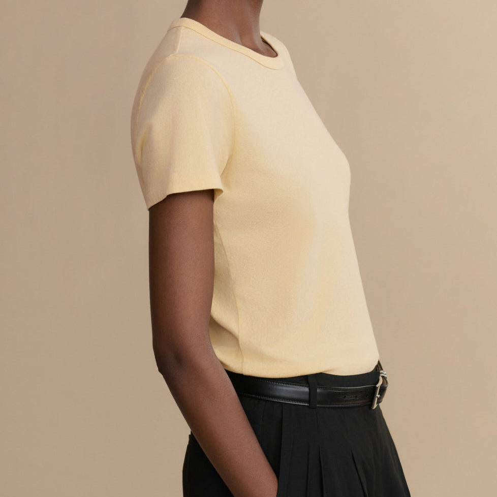Woman wearing a yellow top and black pants against a beige background