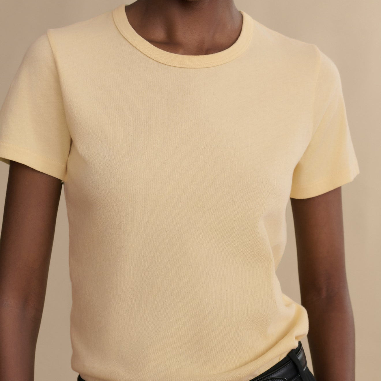 Person wearing a light yellow t-shirt against a beige background