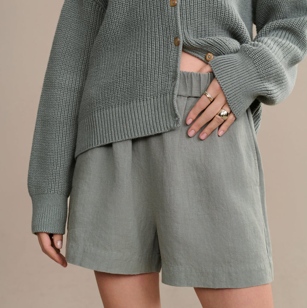 Person wearing a gray knit cardigan and shorts on a beige background