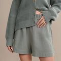 Person wearing a gray knit cardigan and shorts on a beige background