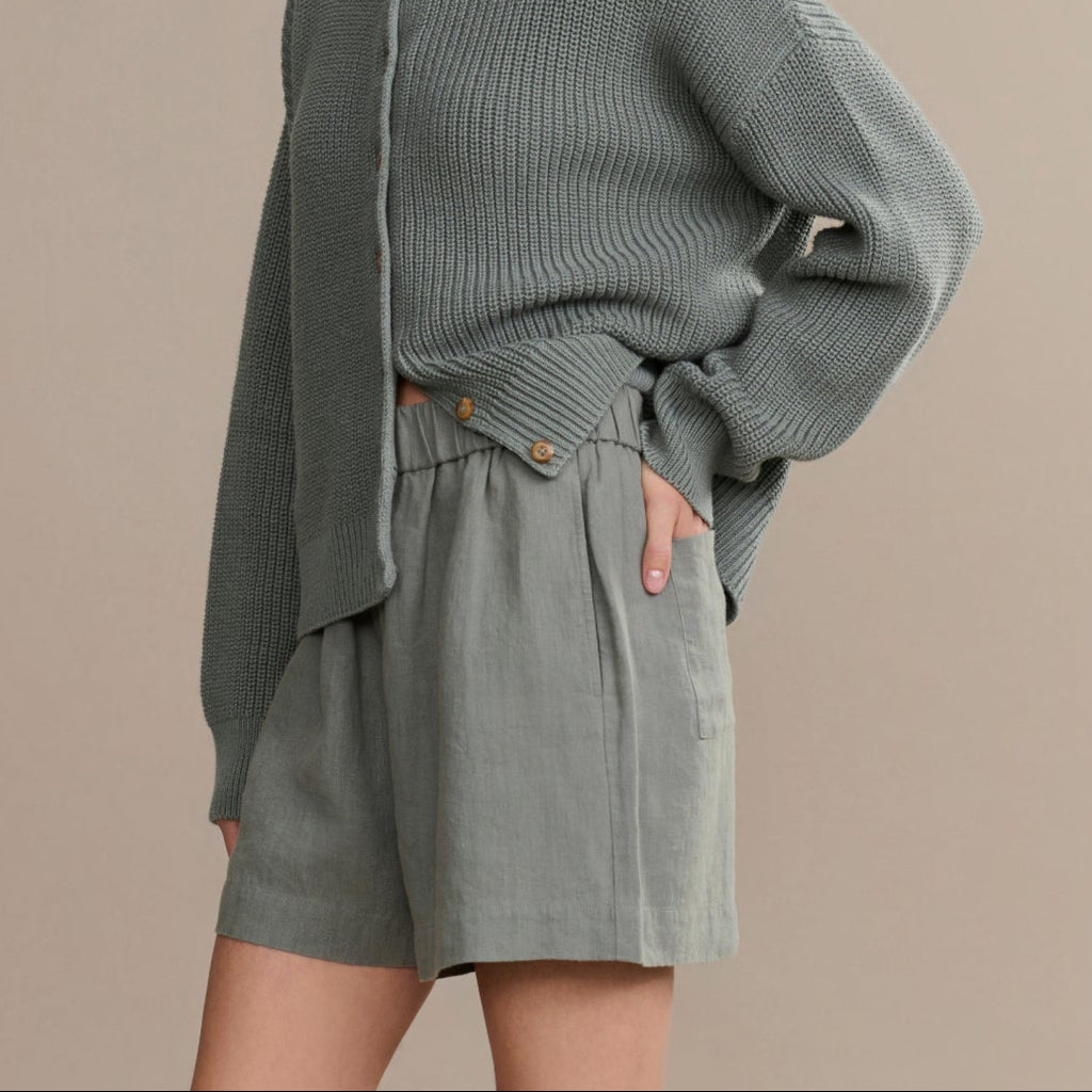 Woman wearing a gray knit cardigan and shorts against a beige background