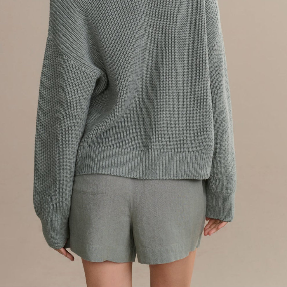 Person wearing a gray sweater and shorts set on a beige background