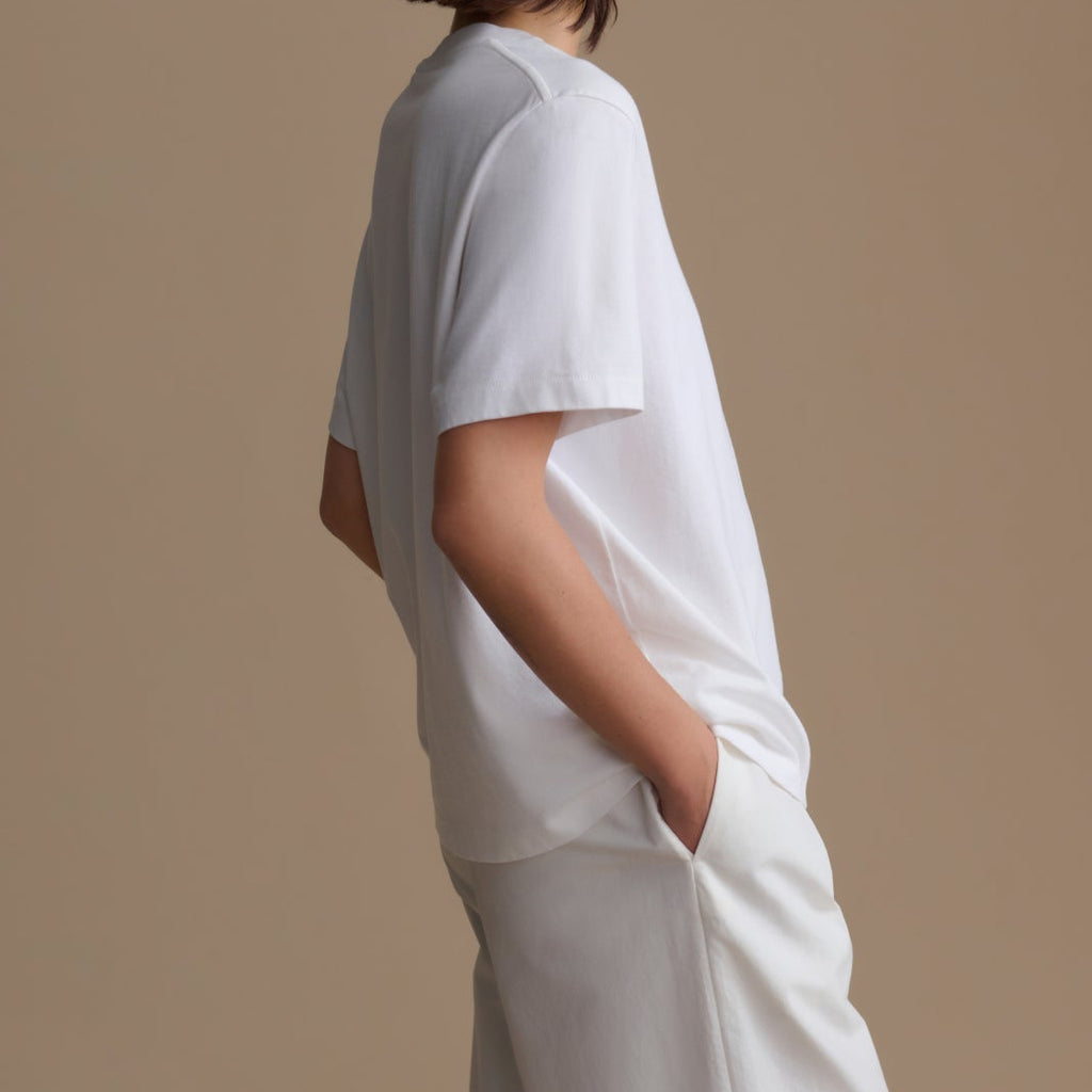 Person wearing a white t-shirt and pants against a beige background