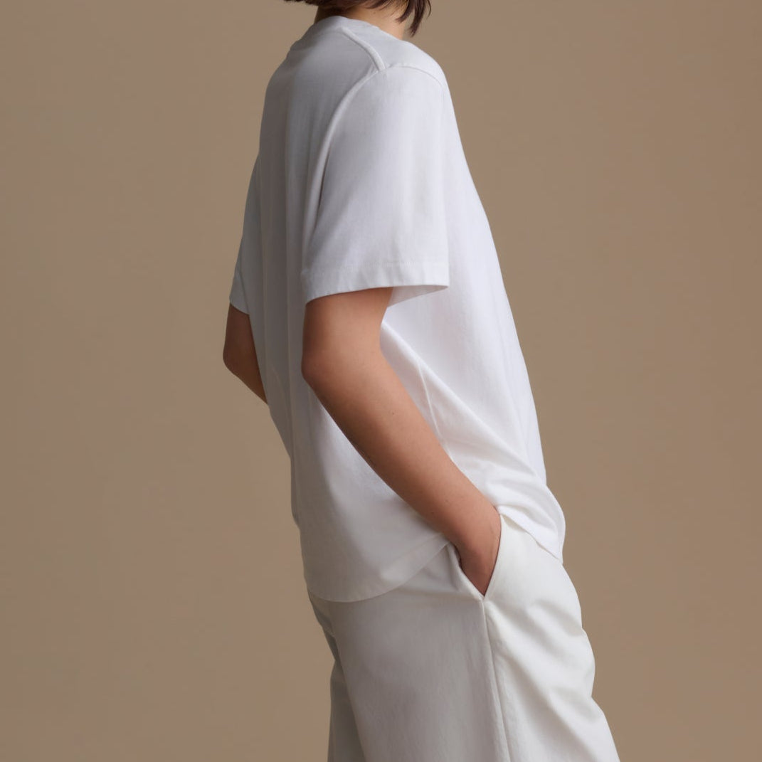 Person wearing a white t-shirt and pants against a beige background