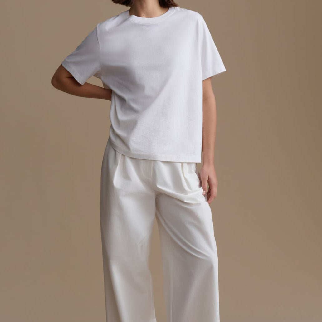 Person wearing a white t-shirt and pants on a beige background