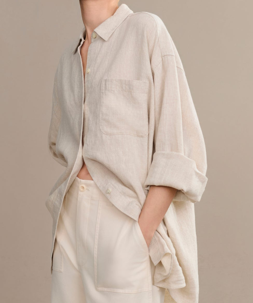 Woman wearing a beige linen shirt and pants against a plain background
