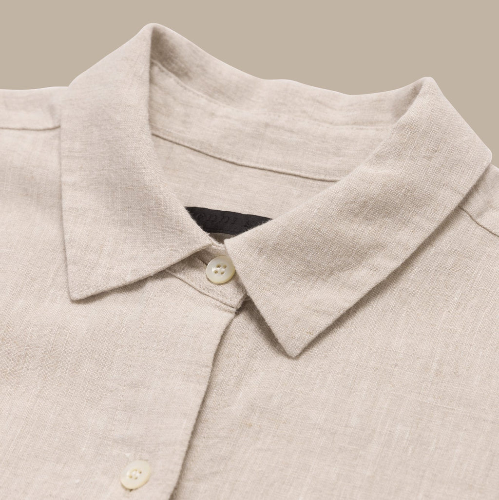 Close-up of a beige shirt collar with buttons on a neutral background