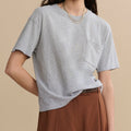 Woman wearing a gray t-shirt with a pocket on a beige background