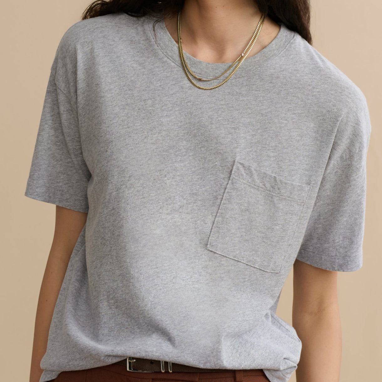 Woman wearing a gray t-shirt with a pocket on a beige background