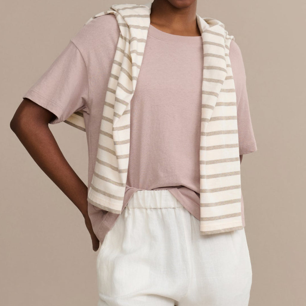 Woman wearing a pink top, white pants, and a striped beige and white cardigan against a beige background