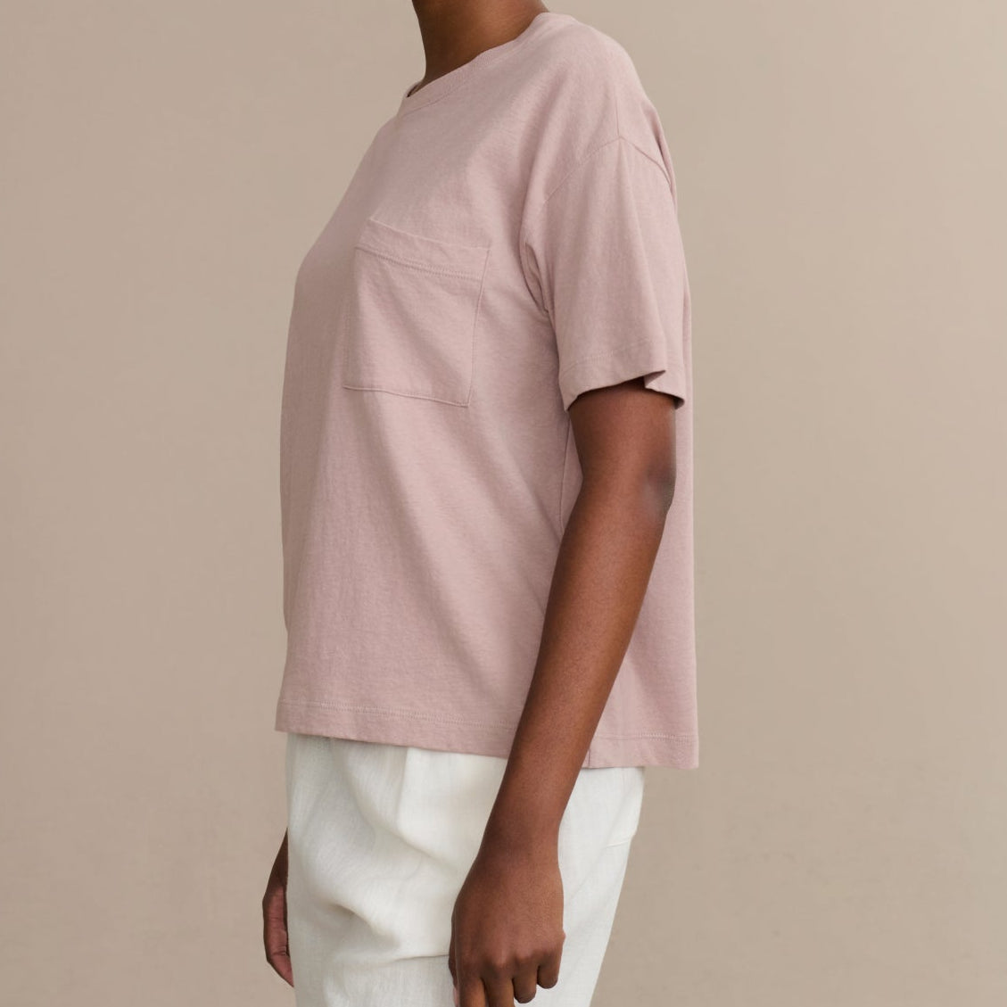 Woman wearing a light pink t-shirt and white pants against a beige background