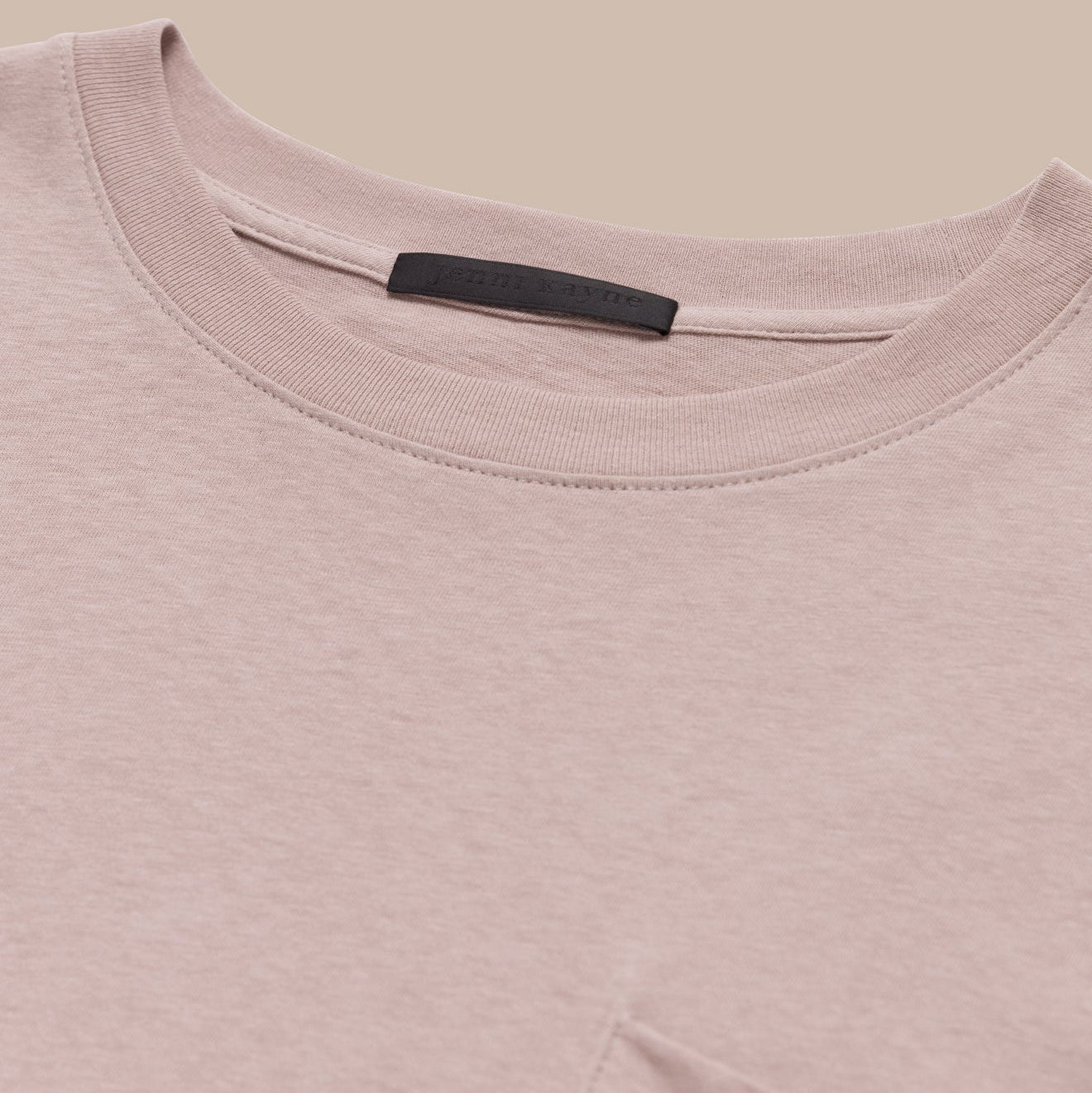 Close-up of a pink t-shirt with a brand label on a beige background