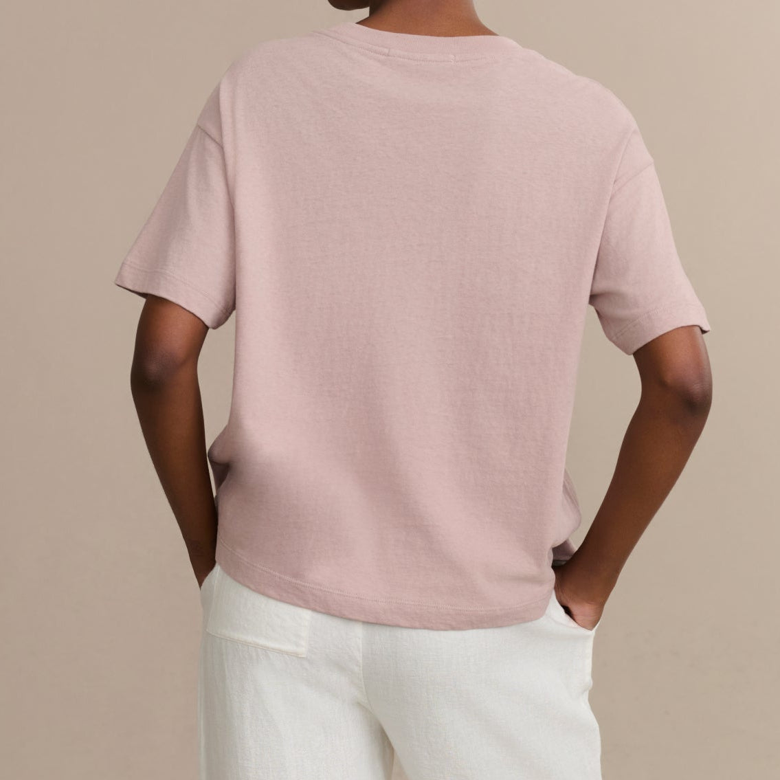 Person wearing a light pink t-shirt and white pants against a beige background