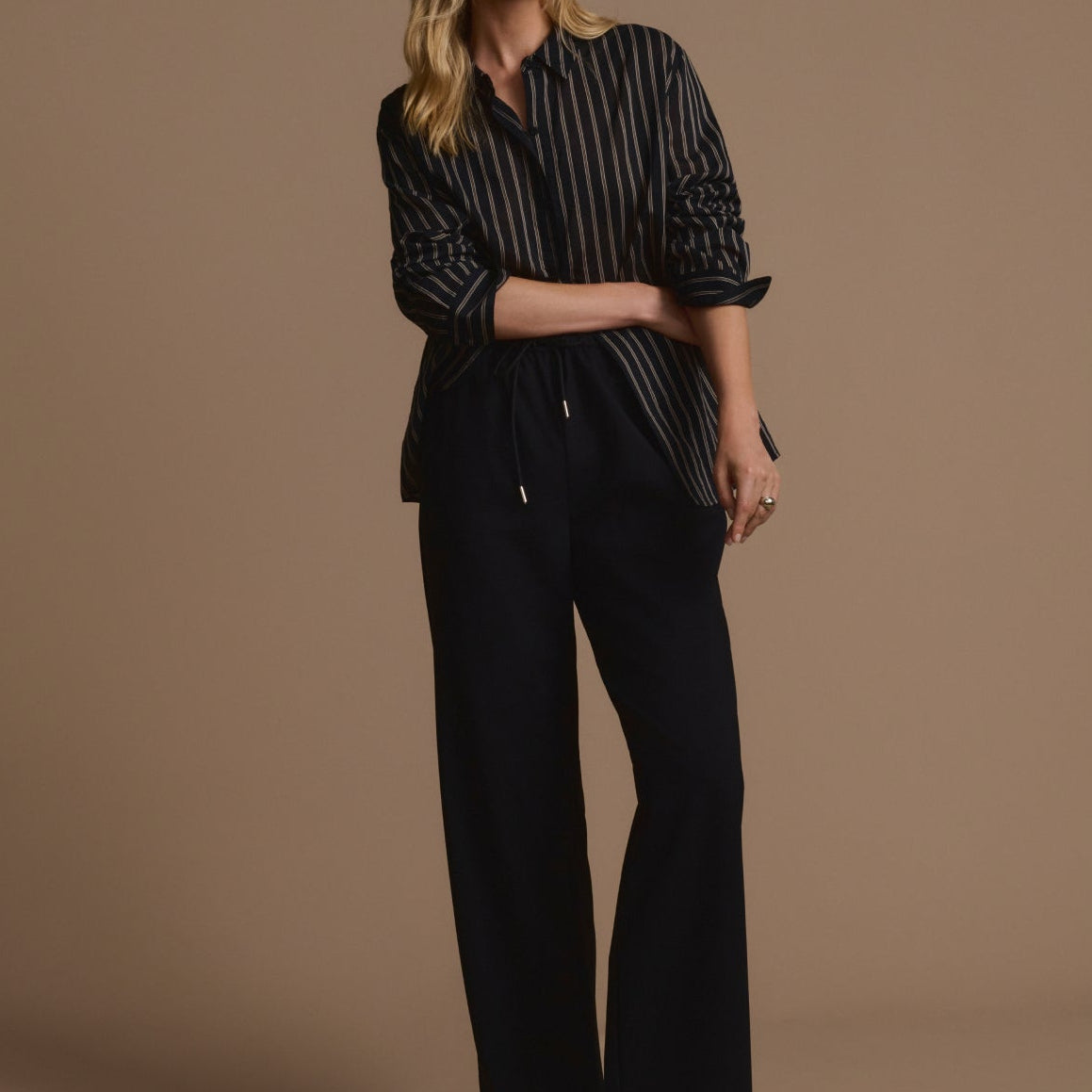 Woman wearing a black striped shirt and black pants against a brown background