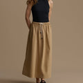 Woman wearing a black top and beige skirt against a brown background