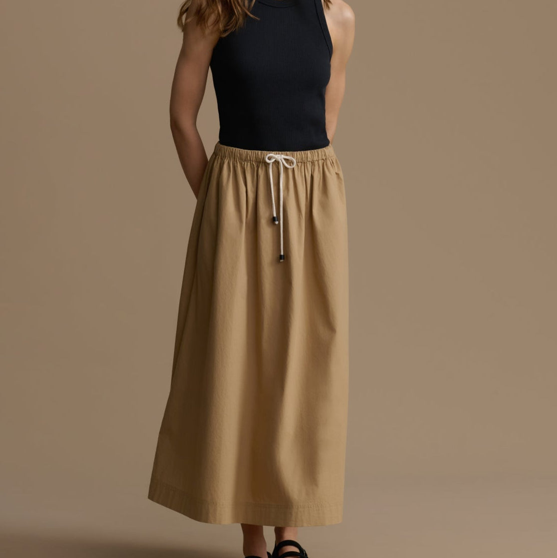 Woman wearing a black top and beige skirt against a brown background