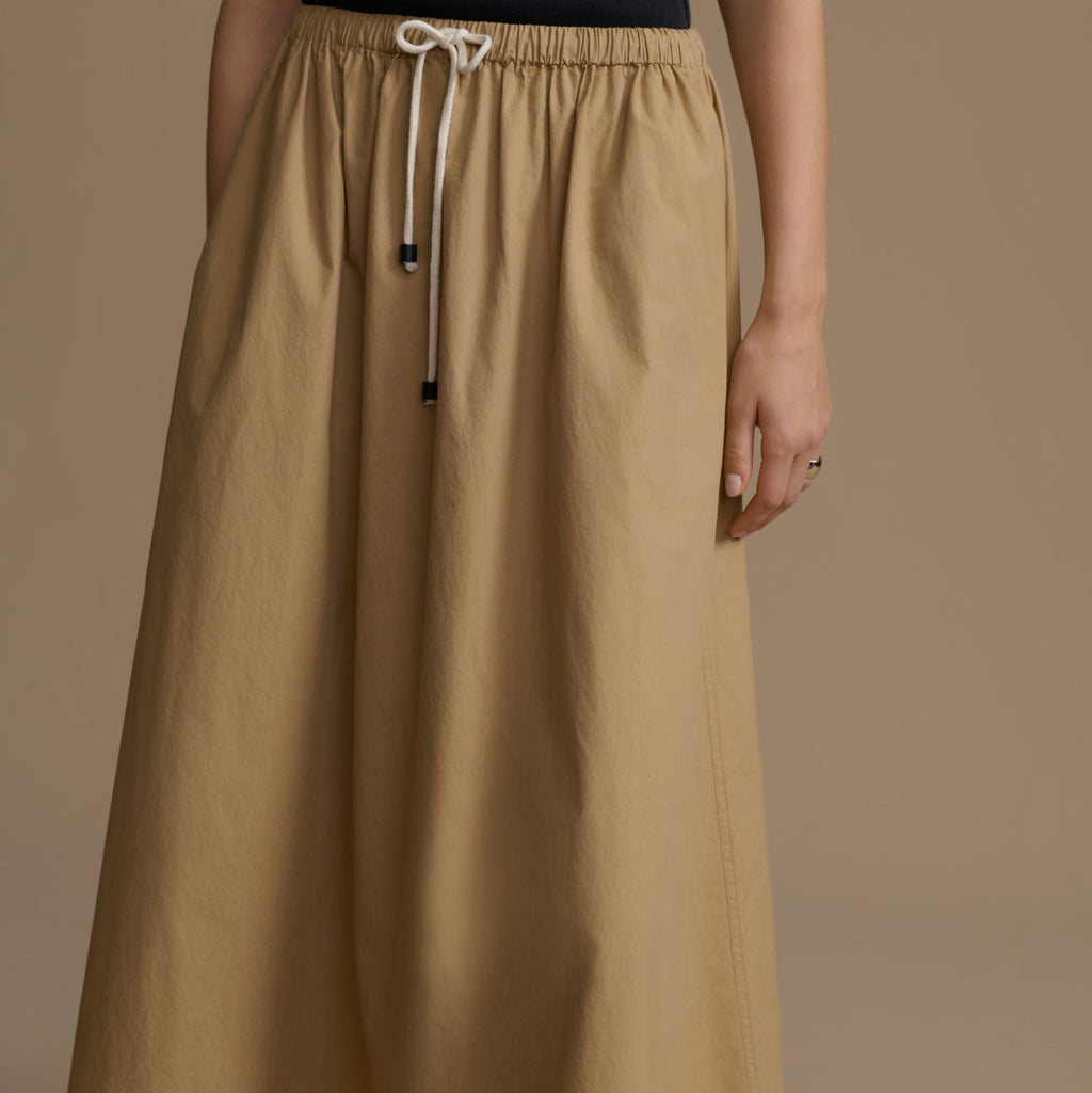 Person wearing a long beige skirt with a plain background