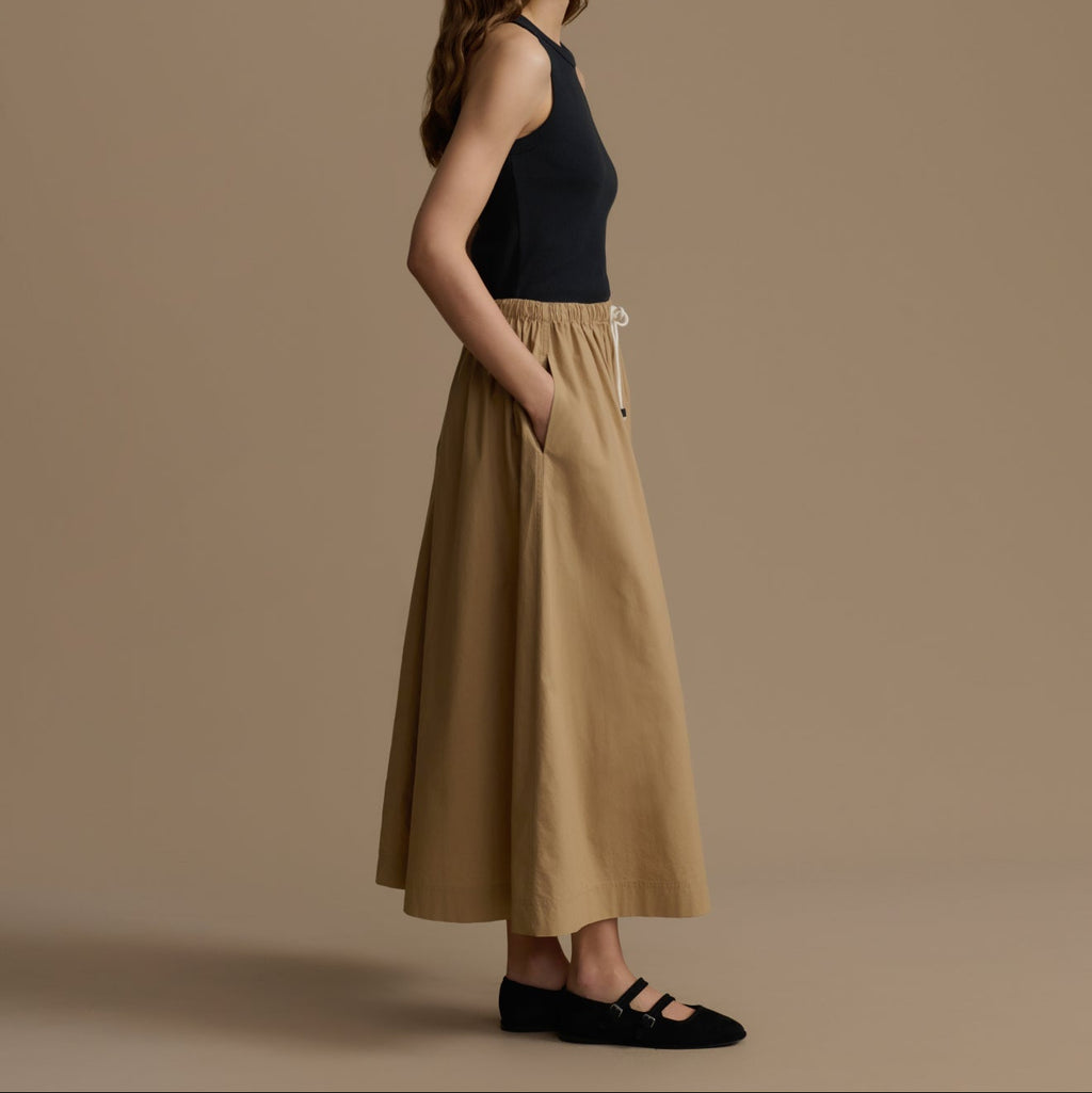 Woman wearing a black top and beige pants against a brown background