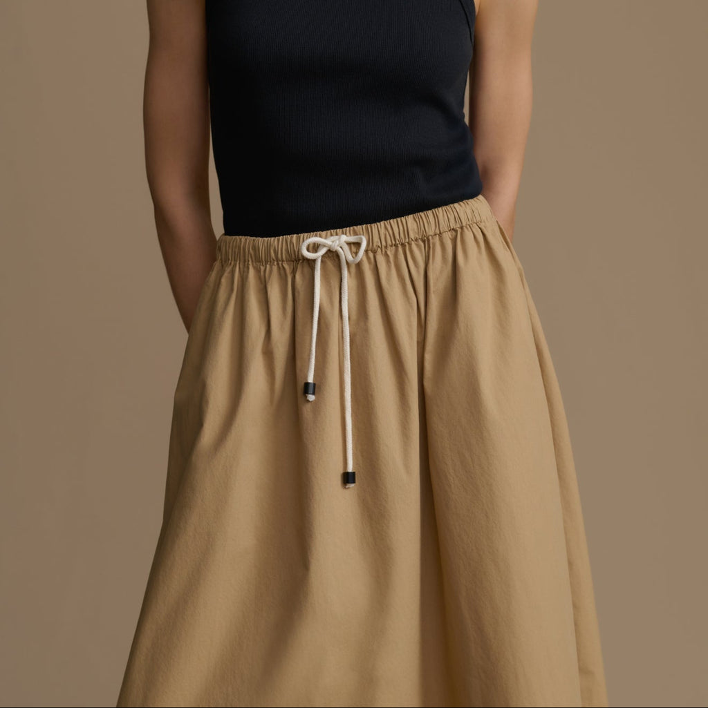 Person wearing a black sleeveless top and tan drawstring pants on a brown background