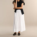 Woman wearing a black top and white skirt against a beige background