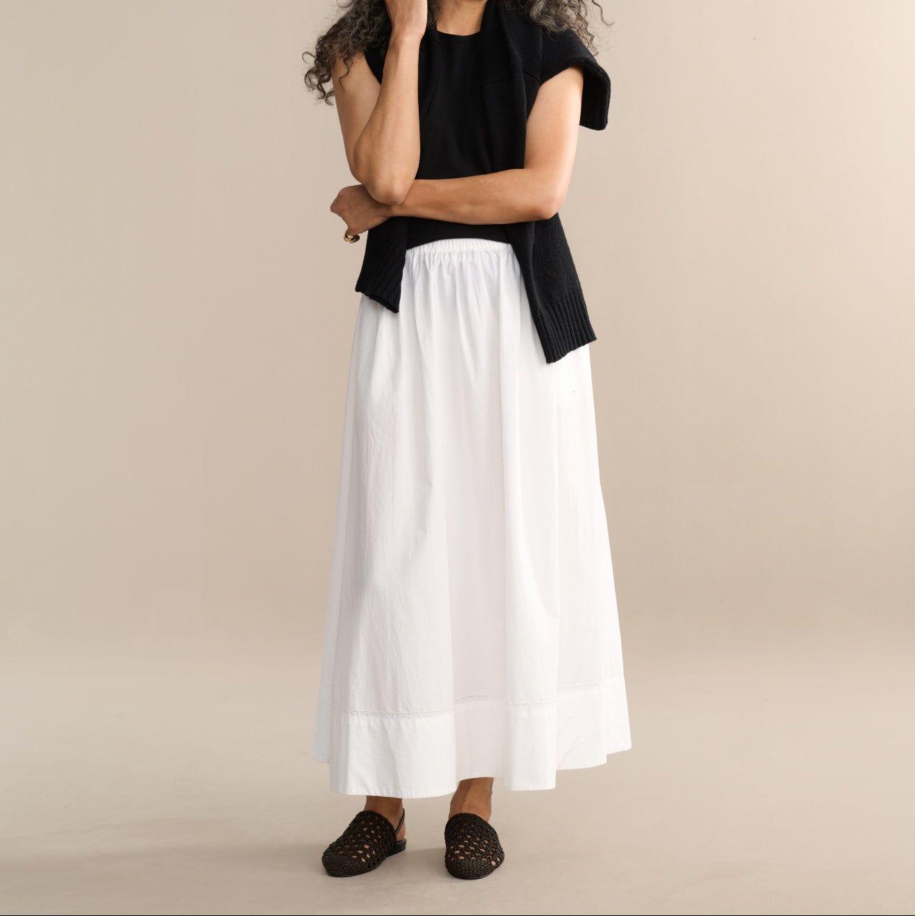Woman wearing a black top and white skirt against a beige background
