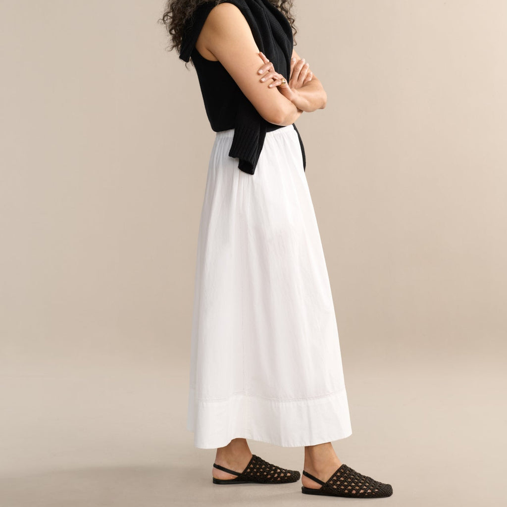 Woman wearing a black sleeveless top and white skirt against a beige background