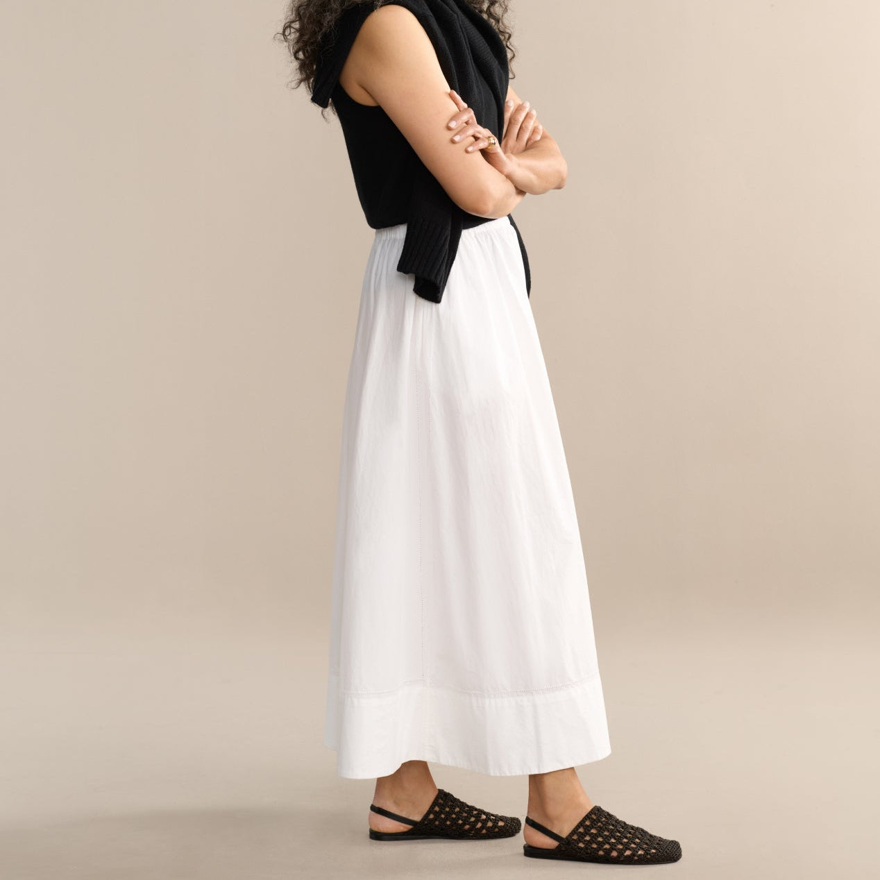 Woman wearing a black sleeveless top and white skirt against a beige background