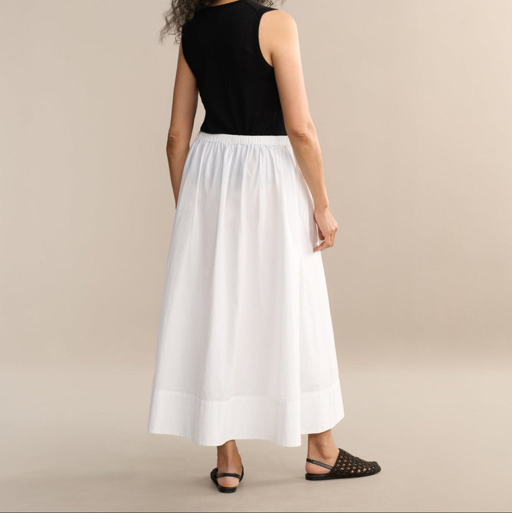 Woman wearing a black top and white skirt on a beige background
