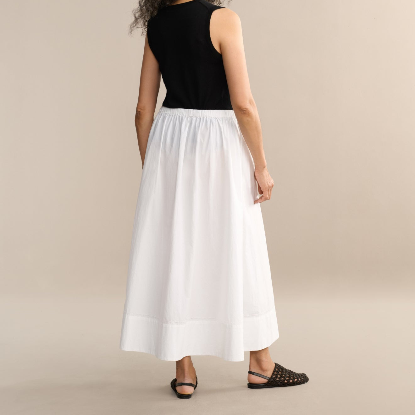 Woman wearing a black top and white skirt on a beige background