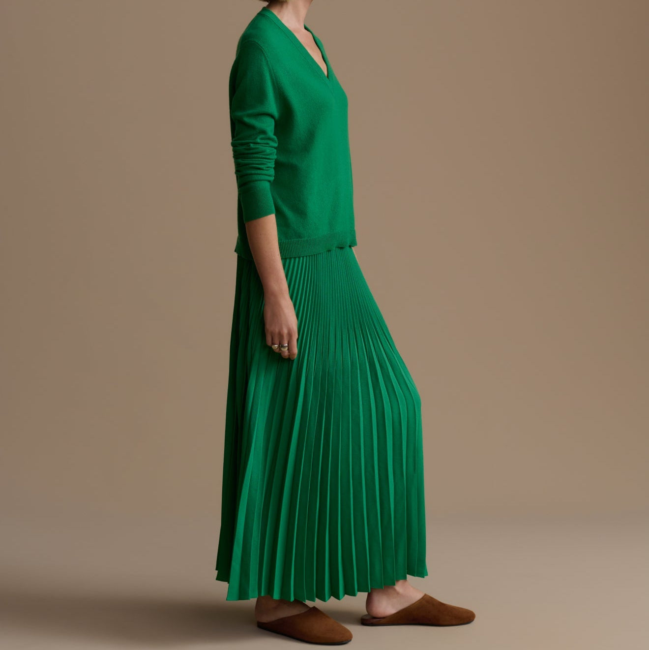 Woman wearing a green pleated skirt and matching top against a beige background