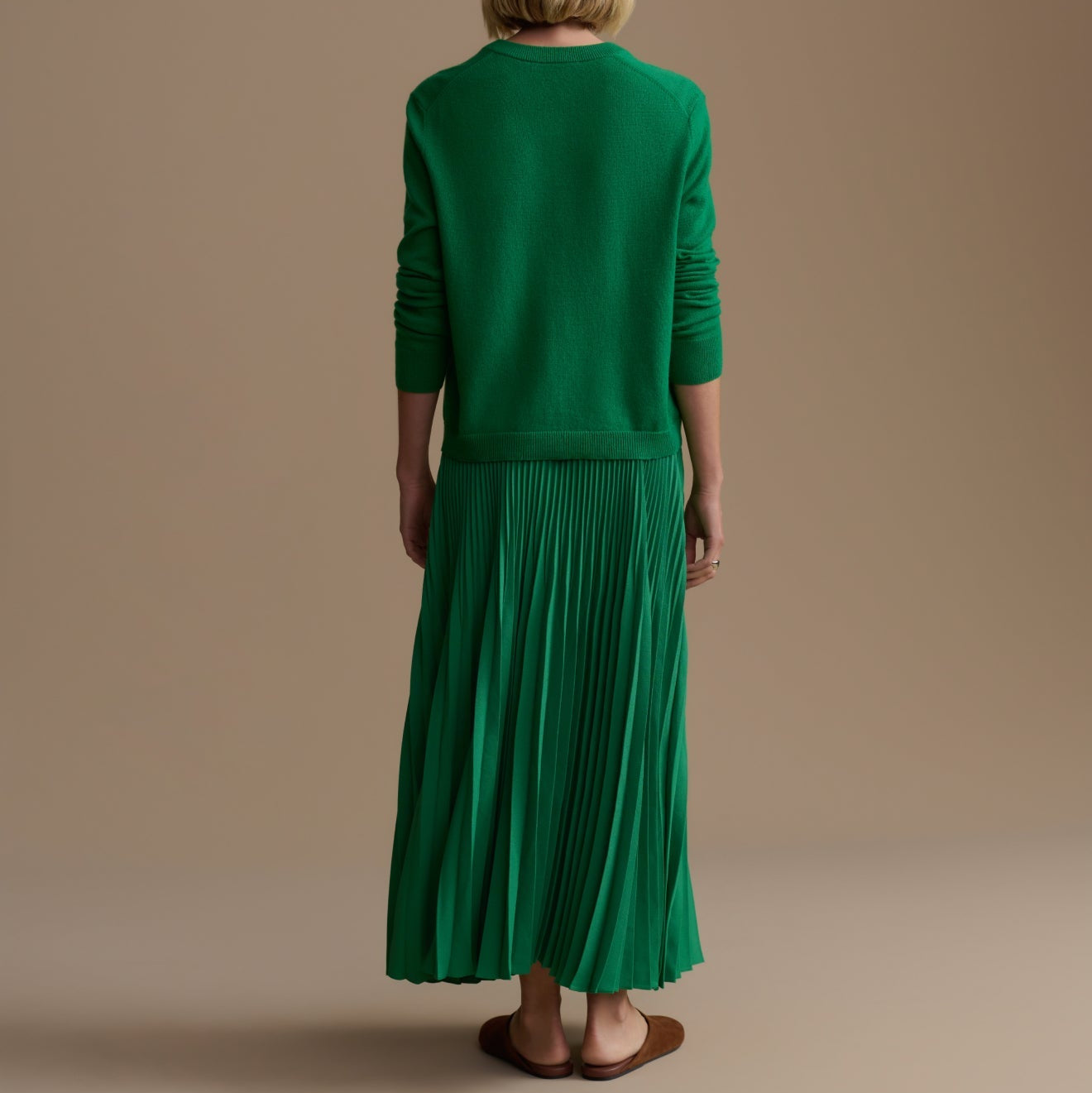 Person wearing a green outfit standing against a beige background