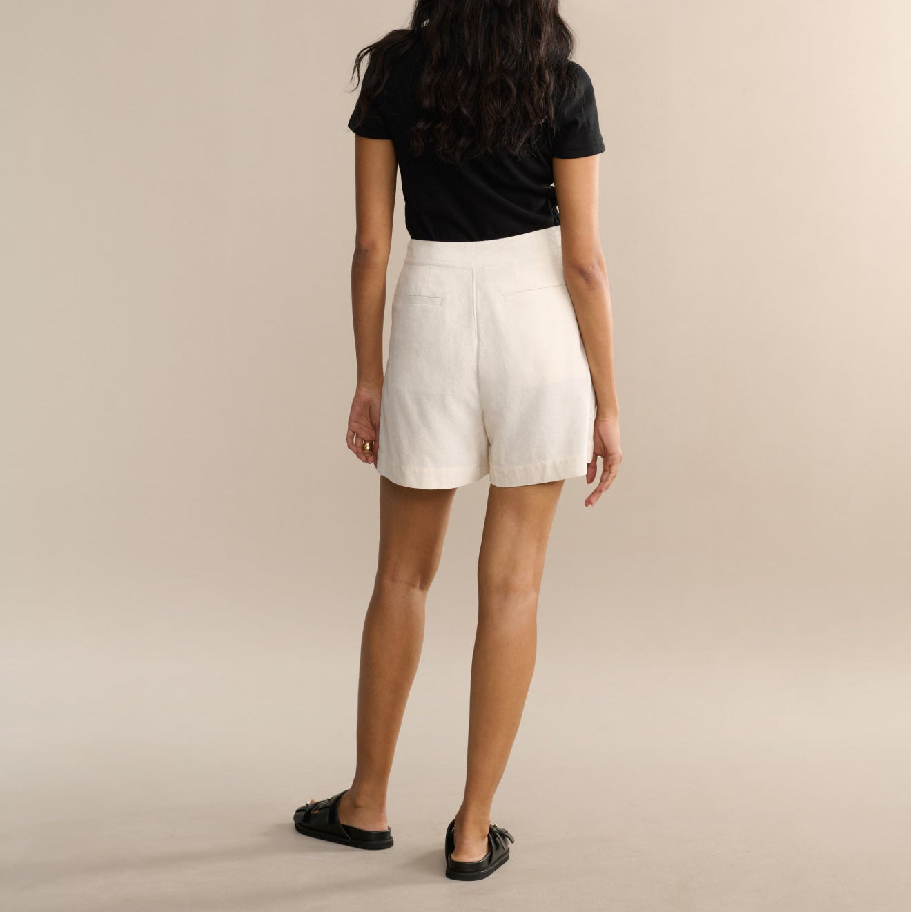 Person wearing a black top and white shorts on a beige background