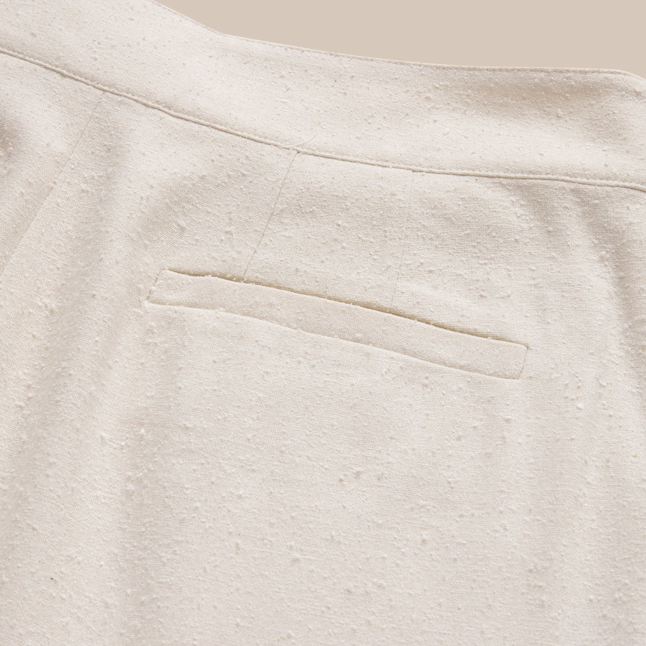 Close-up of a textured beige fabric with a pocket detail.
