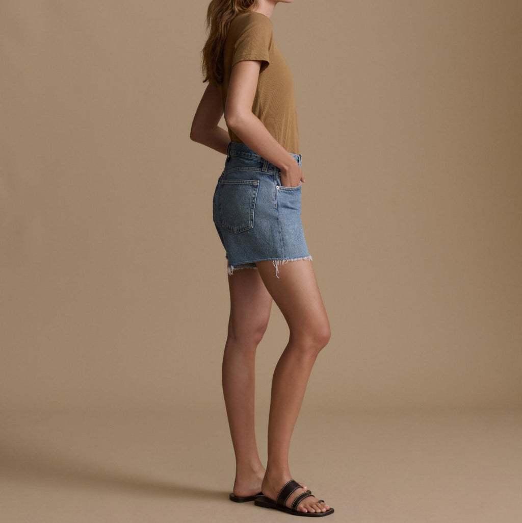 Woman wearing a brown t-shirt and denim skirt on a beige background