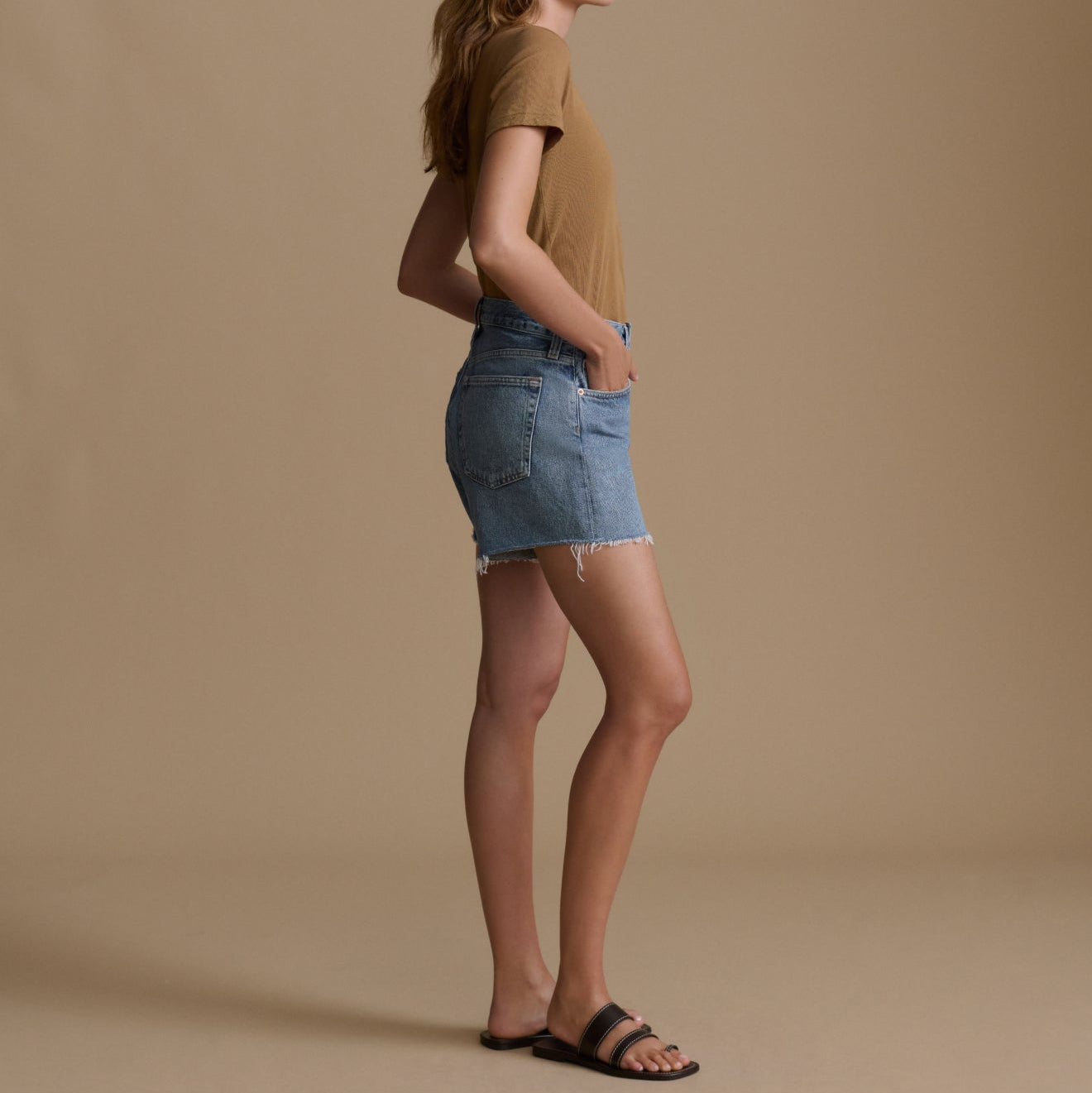 Woman wearing a brown t-shirt and denim skirt on a beige background