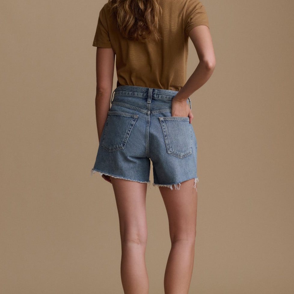 Woman wearing a brown shirt and denim shorts on a beige background